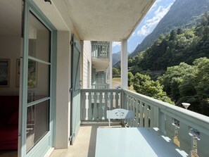 Ein Balkon mit Tisch und Stühlen, mit Blick auf eine gebirgige Landschaft mit üppiger Vegetation.