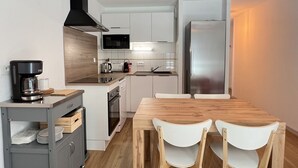 Una cocina moderna con armarios blancos, una campana extractora negra, un refrigerador de acero inoxidable y una mesa de comedor de madera con dos sillas blancas.