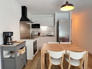 Eine moderne Küche mit weißen Schränken, einer schwarzen Dunstabzugshaube, einem Edelstahlkühlschrank und einem Holzespeisetisch mit zwei weißen Stühlen.