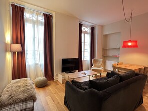 A living room with a sofa, a television, a lamp, and a dining area with a table and chairs. - Charmant T3 - Cœur de Cauterets (Cauterets)
