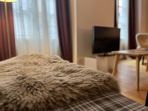 Een kamer met een poef bekleed met bont, een televisie op een standaard en een stoel.
