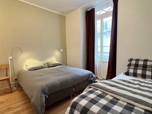 Un dormitorio con cama, mesita de noche, lámpara y ventana con cortinas.