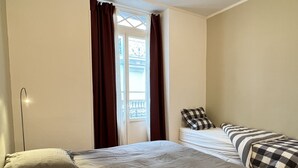 A room with a bed, a bedside table, and a window with curtains. - Charmant T3 - Cœur de Cauterets (Cauterets)