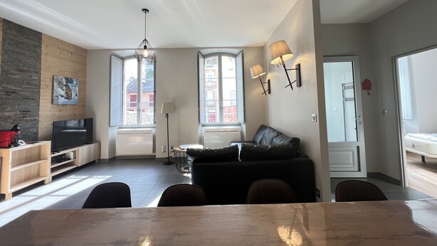 A modern living room with a dining table, black leather sofa, and a TV.