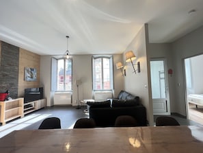 Una sala de estar moderna con comedor, un sofá de cuero negro, una mesa de comedor de madera y un televisor.