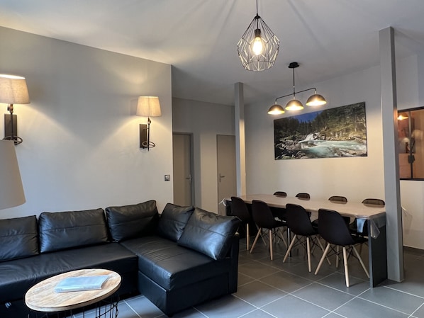 Una sala de estar moderna con un sofá de cuero negro, una mesa de centro redonda y un comedor con una mesa larga y sillas.