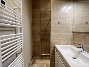Un baño con una bañera blanca, cabina de ducha de vidrio y paredes con azulejos color beige.