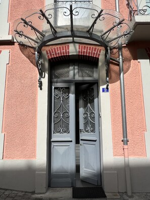 A building entrance with a double door featuring decorative metalwork, a small balcony with a metal railing, and a blue parking sign. - Joli T3 rénové ds une villa 1900 (Cauterets)