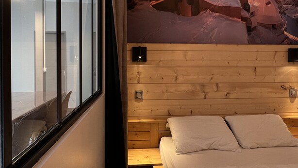 Une pièce avec un lit, un lambris en bois, une fenêtre et une affiche représentant un paysage enneigé.