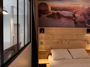 Una habitación con una cama, pared de paneles de madera, una ventana y un cartel de un paisaje nevado.