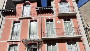 A multi-story building with a red facade, multiple windows, and balconies with wrought iron railings.