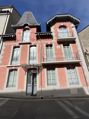 A multi-story building with a red facade, multiple windows, and balconies with wrought iron railings.