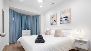 A modern hotel room with a large bed, a bedside table with a lamp, and a wardrobe.
