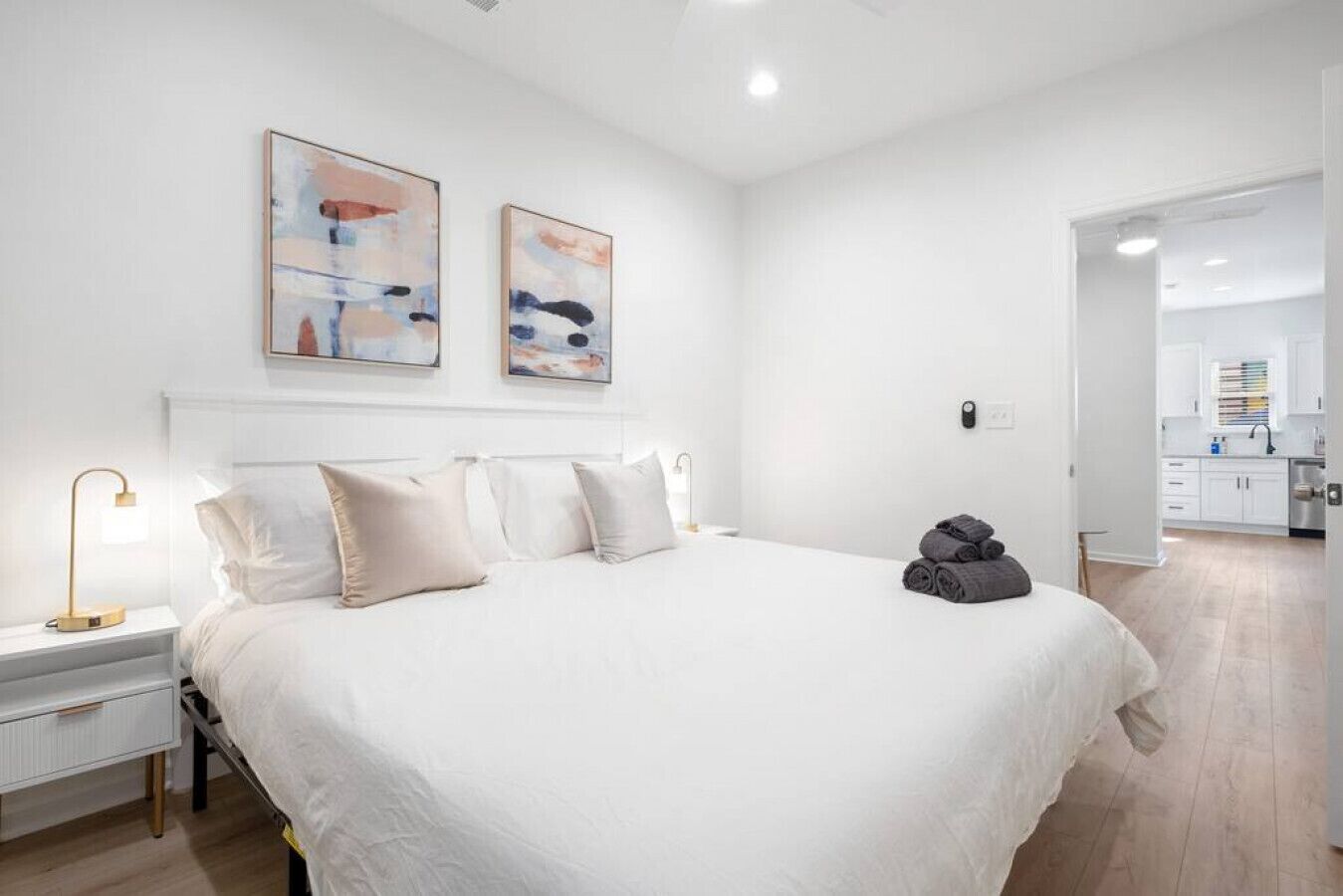 A spacious bedroom with a large bed, a bedside table with a lamp, and abstract artwork on the wall.