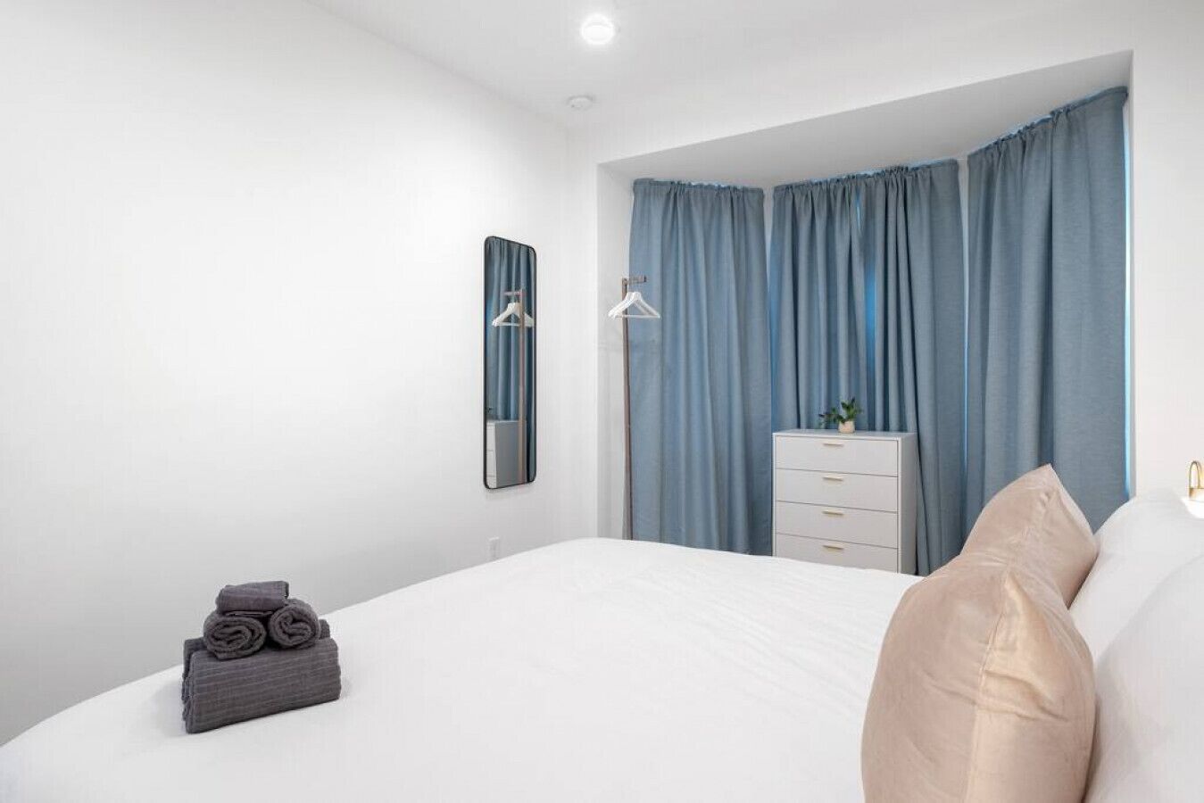 A modern bedroom with a large bed, a dresser, a mirror, and a window with curtains.