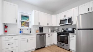 A modern kitchen with white cabinets, stainless steel appliances, and a wooden floor.
