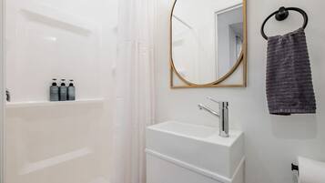 A modern bathroom with a white sink, a mirror with a gold frame, and a towel hanging on a ring.