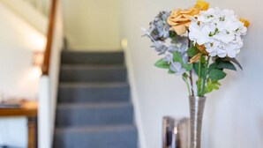 Un vase rempli de fleurs est posé sur une table dans une pièce où se trouve un escalier.