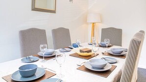 Un coin repas avec des chaises à rayures, une table dressée avec des assiettes, des bols et des verres, et une lampe fixée au mur.