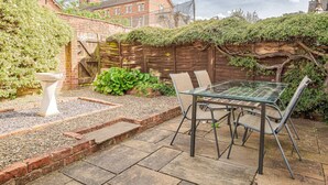 Une terrasse avec une table et des chaises en verre, entourée d’un mur de briques et de verdure.