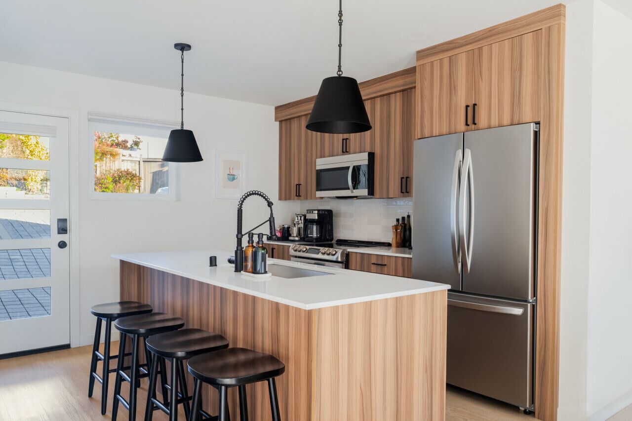 A modern kitchen with wooden cabinets, a stainless steel refrigerator, a microwave, and a bar area with stools.