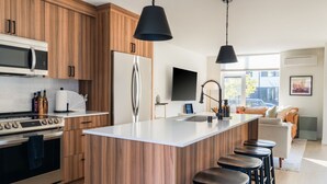 Une cuisine moderne avec des meubles en bois, des appareils électroménagers en acier inoxydable, un îlot central doté de tabourets de bar et une grande fenêtre qui laisse entrer la lumière naturelle.