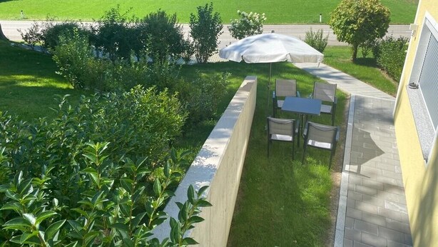 A patio with a table and chairs, a white umbrella, and a view of a green field.
