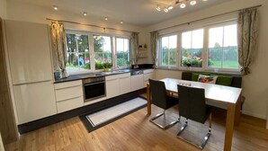 A modern kitchen with a dining area, large windows, and a view of the garden.