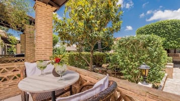 A patio with wicker furniture, a table with drinks, and a tree.