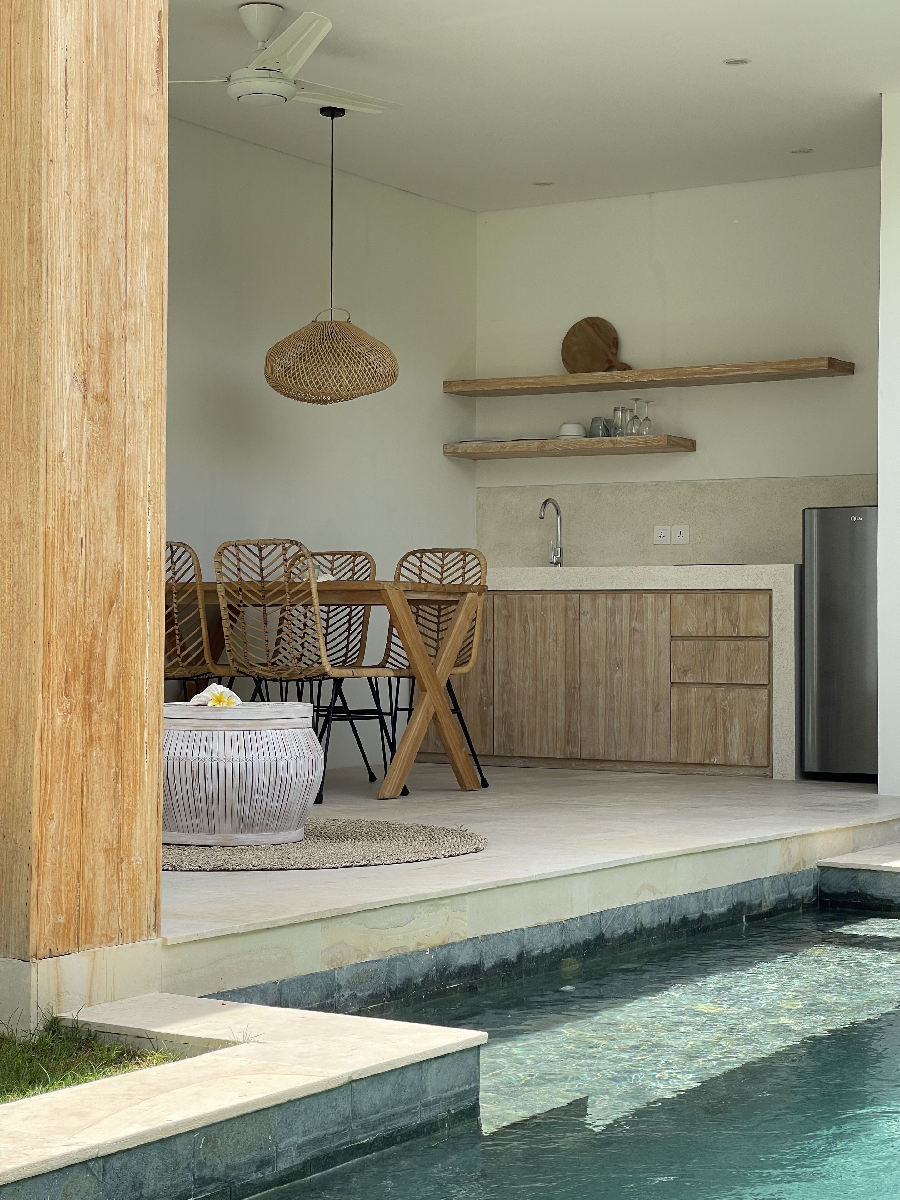 A modern kitchen with wooden cabinets, a stainless steel refrigerator, and a dining area with wicker chairs.