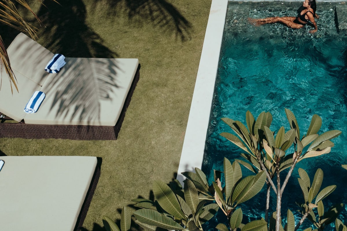 A modern outdoor pool area with a lounge chair, a small table, and a person swimming.