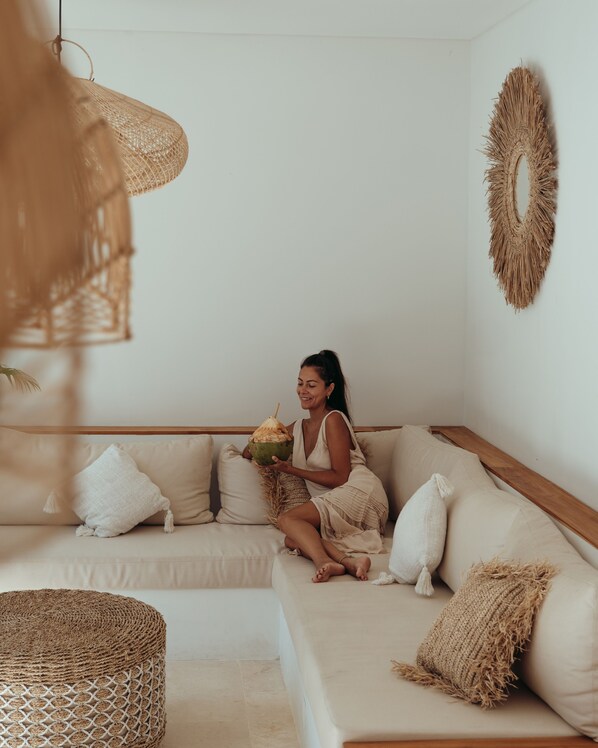 A woman sitting on a beige sofa with a woven basket and a coconut. - Kalea Villas (Kuta)