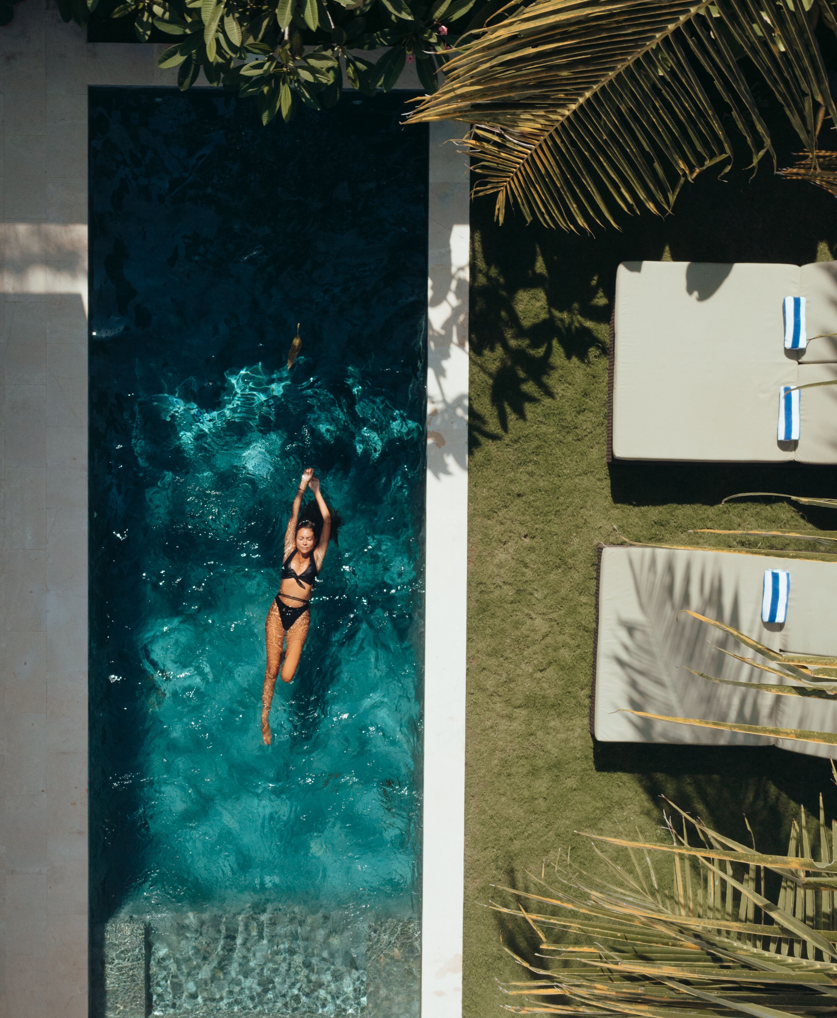 A swimming pool with clear water, a person swimming, and a lounge area with towels and a sun lounger.