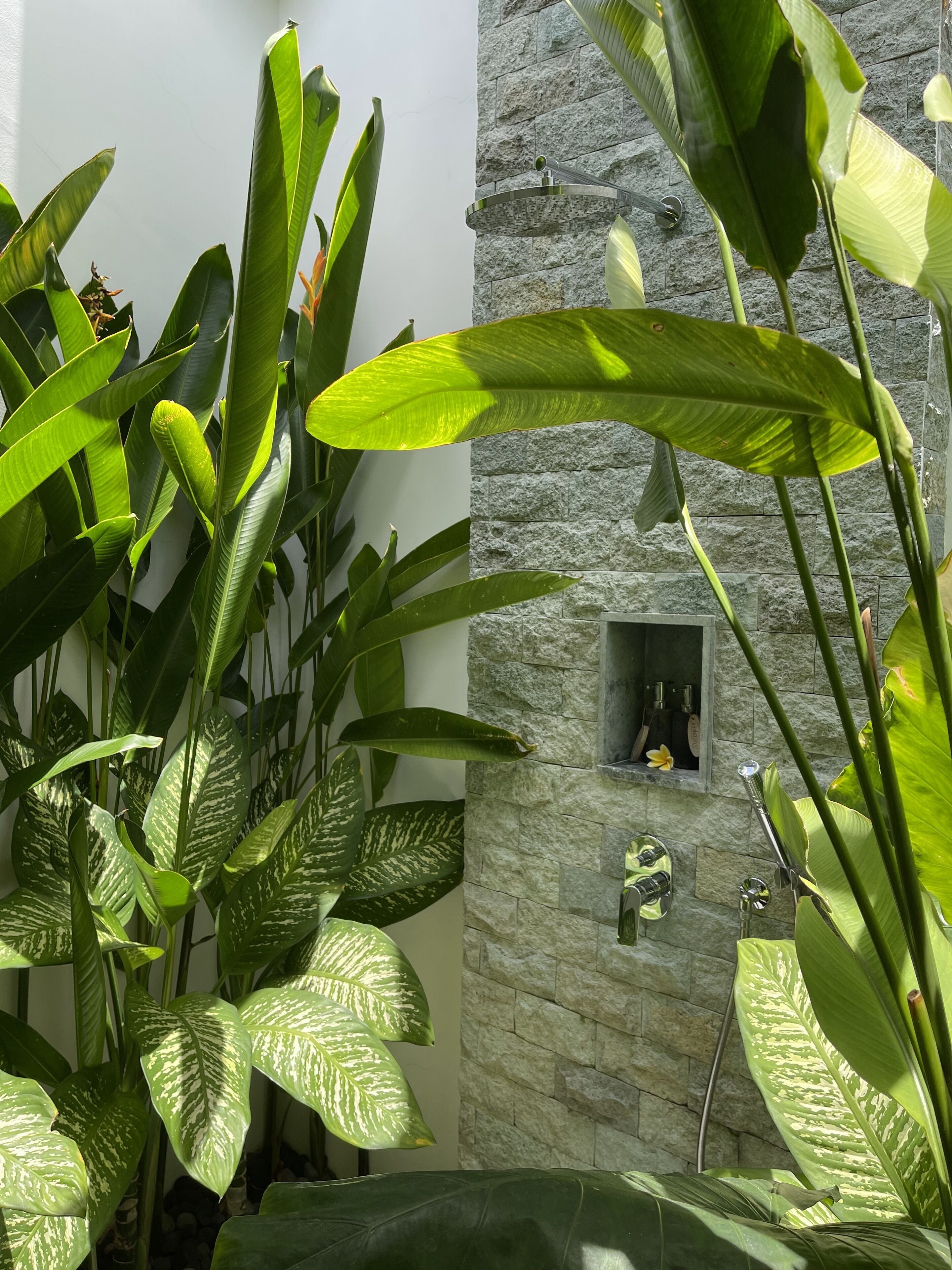 A bathroom with a stone wall, a shower, and a window with a small shelf.