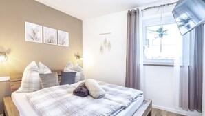 A bedroom with a bed, pillows, a bedside table, wall art, and a window with curtains.
