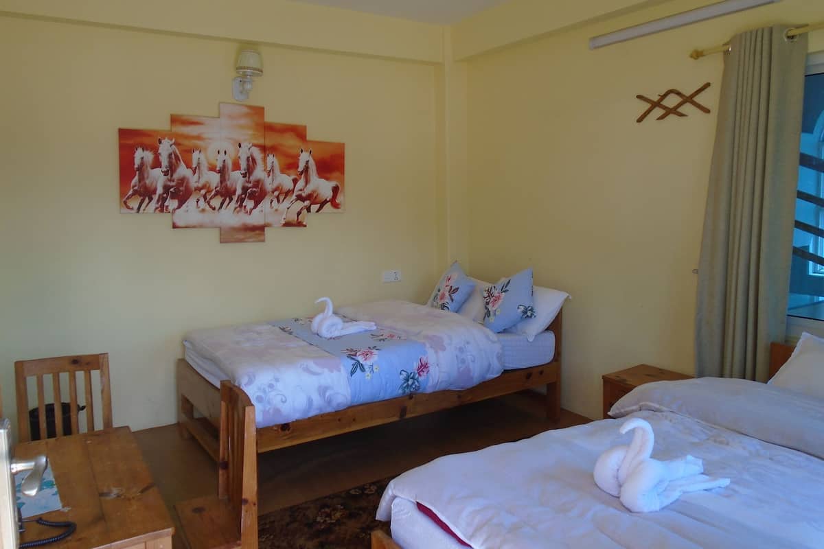 Une chambre d’hôtel avec deux lits en bois, une literie à motifs floraux, un tableau représentant des chevaux, une chaise en bois et un bureau avec un téléphone.