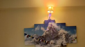 Ein Hotelzimmer mit Bett, Kissen, einer Nachttischlampe und einem Wandbild von einem Berg.