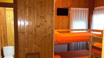 Una habitación de madera con una cama, una silla, un inodoro y un televisor.