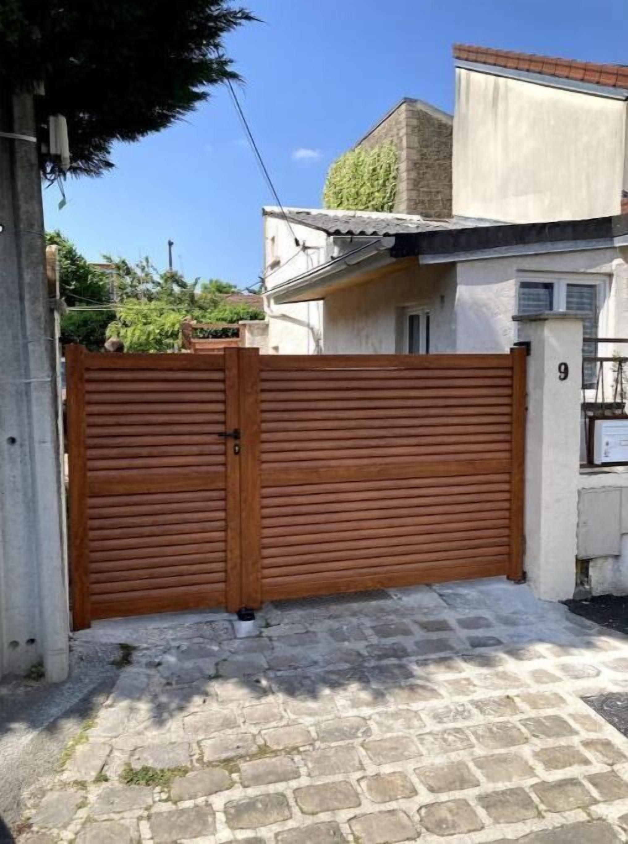Une entrée fermée par un portail en bois, une allée pavée de pierres et un bâtiment doté d’un toit en tuiles et d’une plaque portant le numéro « 9 ».