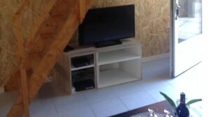 A living room with a wooden staircase, a television on a white stand, and a glass door leading outside. - La Campagne Proche de Paris - Chez Lulu (Montreuil)