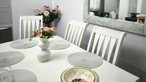 A dining area with a white table, grey placemats, white chairs, and a vase with flowers. - Vacation Home "Marilidia House" with 2 Balconies, Shared Terrace & Wi-Fi (Kastelli)