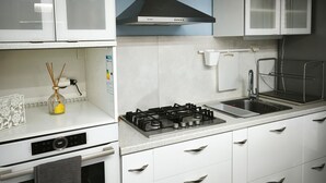 A modern kitchen with white cabinets, a stainless steel range hood, a gas stove, a sink, and a chair. - Vacation Home "Marilidia House" with 2 Balconies, Shared Terrace & Wi-Fi (Kastelli)