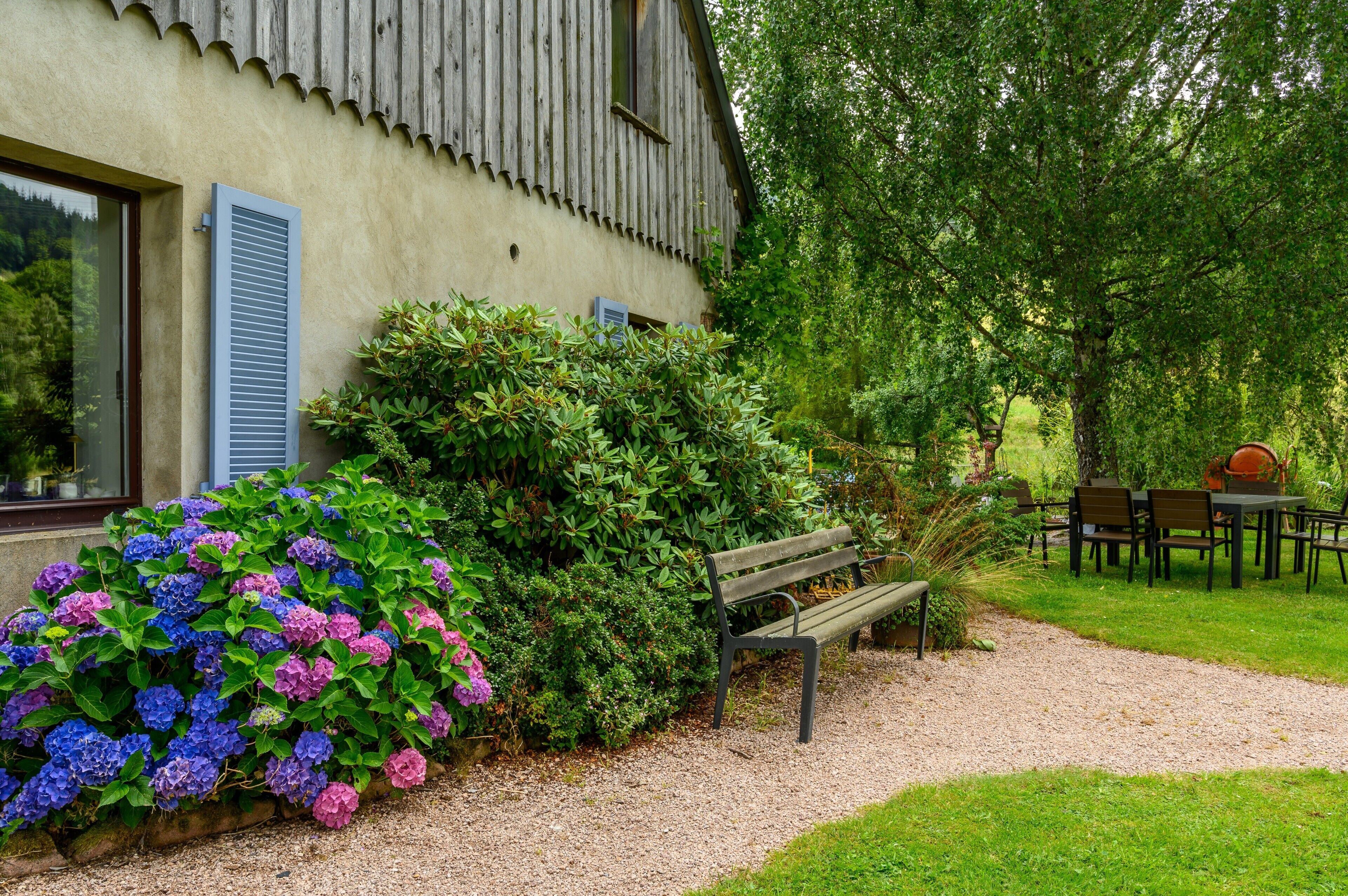 Un bâtiment rustique avec un chemin de gravier, un banc et une table entourée de chaises.