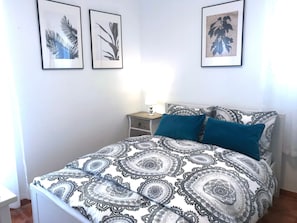 Un dormitorio con una cama, una mesita de noche e imprime botánicas enmarcadas en la pared.