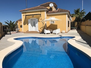 Una piscina con borde de azulejos, una casa con techo de tejas y una antena parabólica.