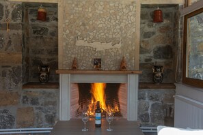 Ein Kamin aus Stein mit Feuer, eine Weinflasche und zwei Gläser auf einem Tisch.