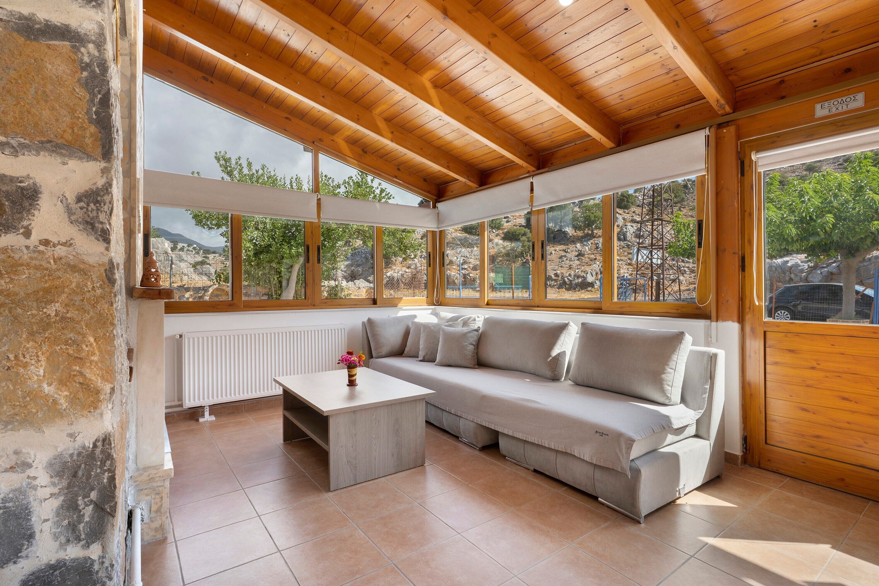 Une pièce avec un plafond en bois, une grande fenêtre, un canapé, une petite table et un radiateur.
