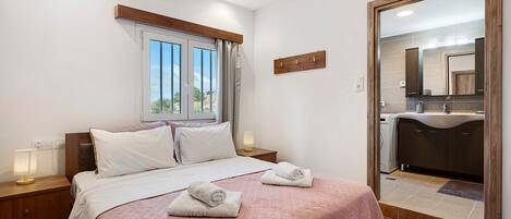 A bedroom with a bed, bedside tables, a window, and a bathroom visible through an open door.