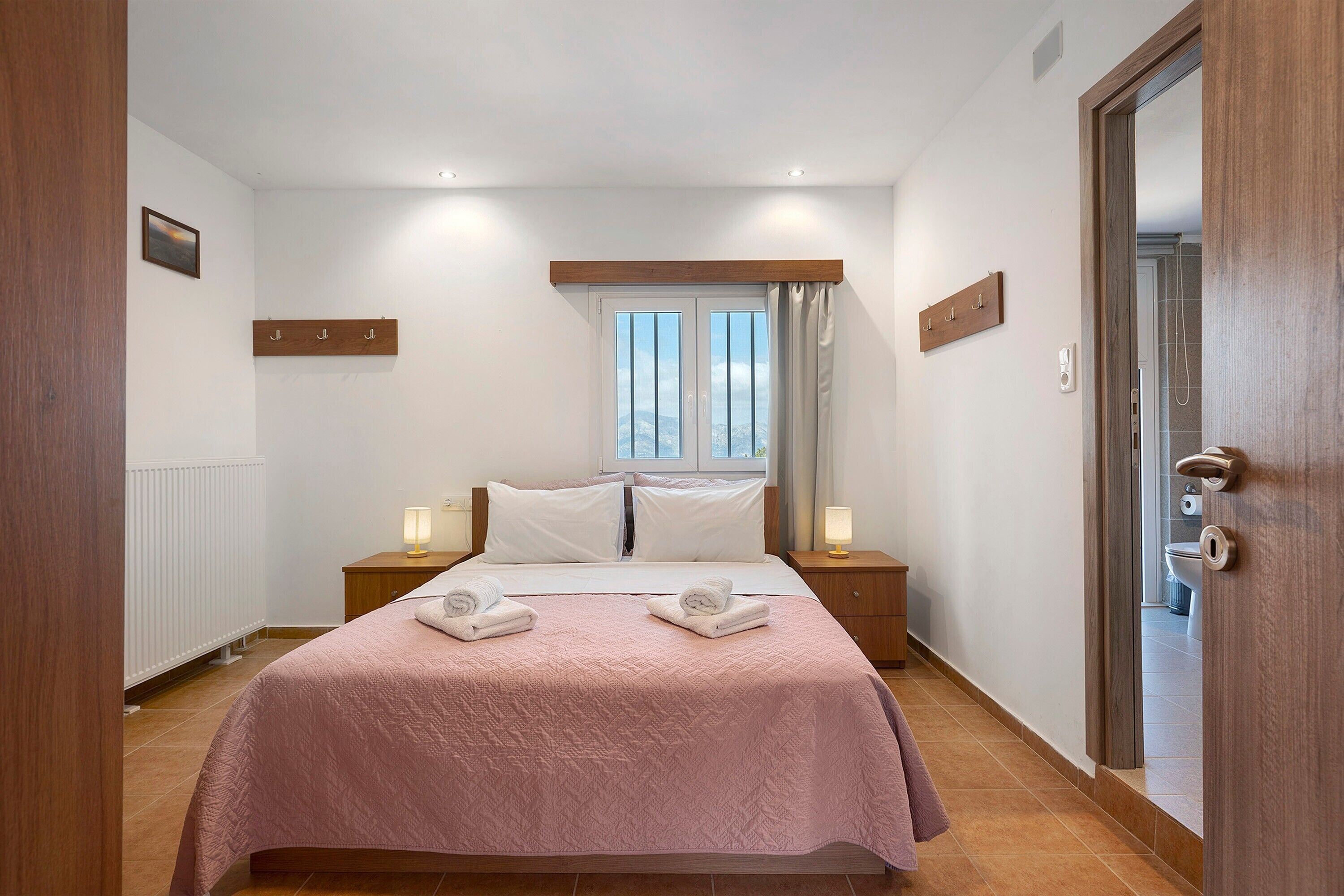 Une chambre à coucher avec un lit, deux tables de chevet avec des lampes, une fenêtre avec des rideaux et un radiateur.