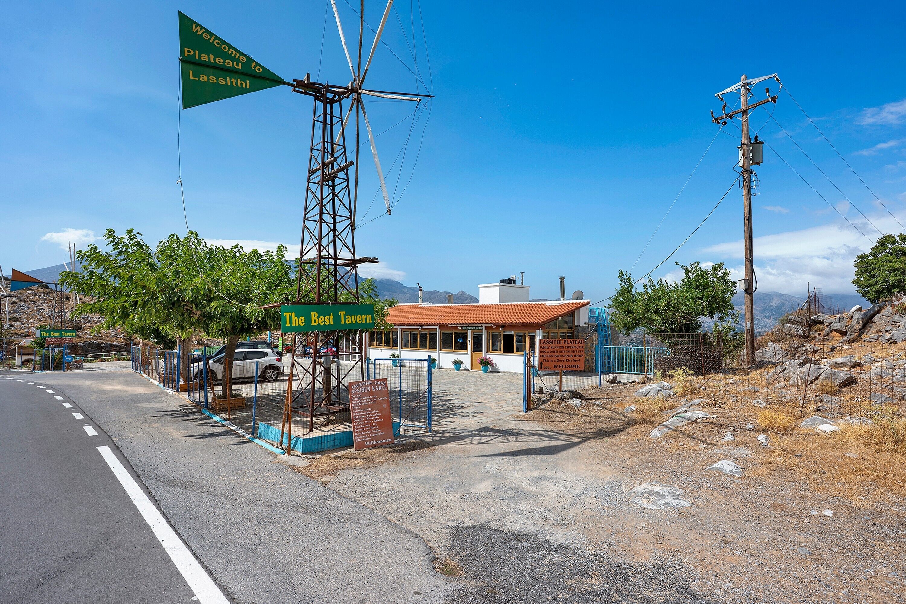 Une route mène à une taverne familiale, et une pancarte souhaite la bienvenue aux visiteurs sur le plateau de Lassithi.